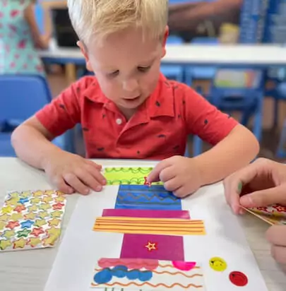 Child in a red polo placing stickers on a piece of paper with blocks of different colors on it.