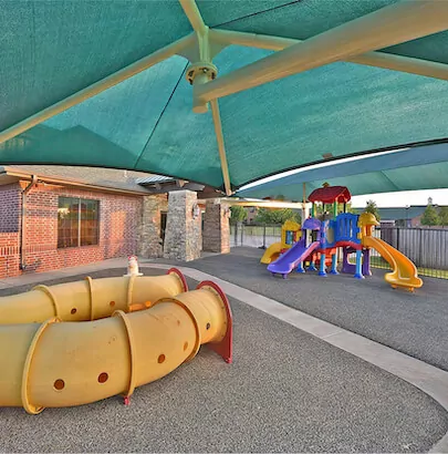 Colorful playground with a yellow tube slide on the ground and a green semi-opaque shade over the top.