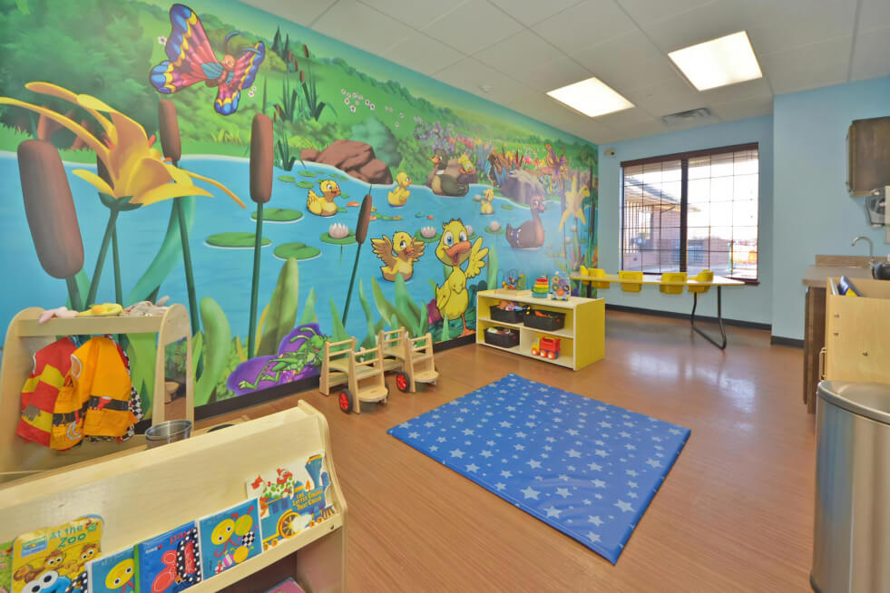 Classroom with a blue mat with a star pattern on the floor and a mural of ducks in a pond on one wall.