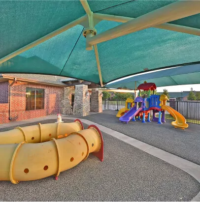 Colorful playground with a yellow tube slide on the ground and a green semi-opaque shade over the top.