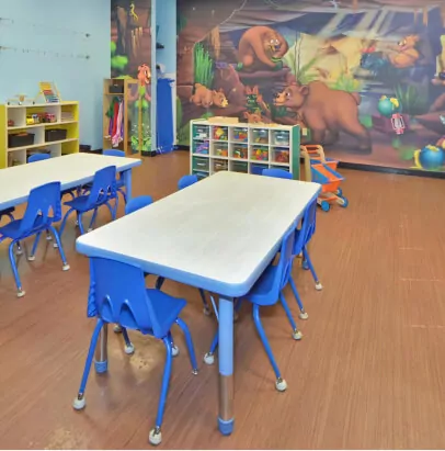 Classroom with rectangular tables with blue plastic chairs around them. On one of the walls, there's a mural of bears in a cave.