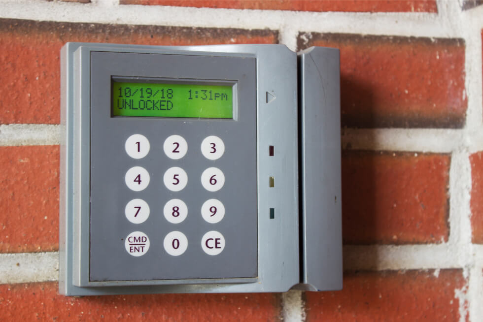A keypad with a green screen affixed to a red brick wall.