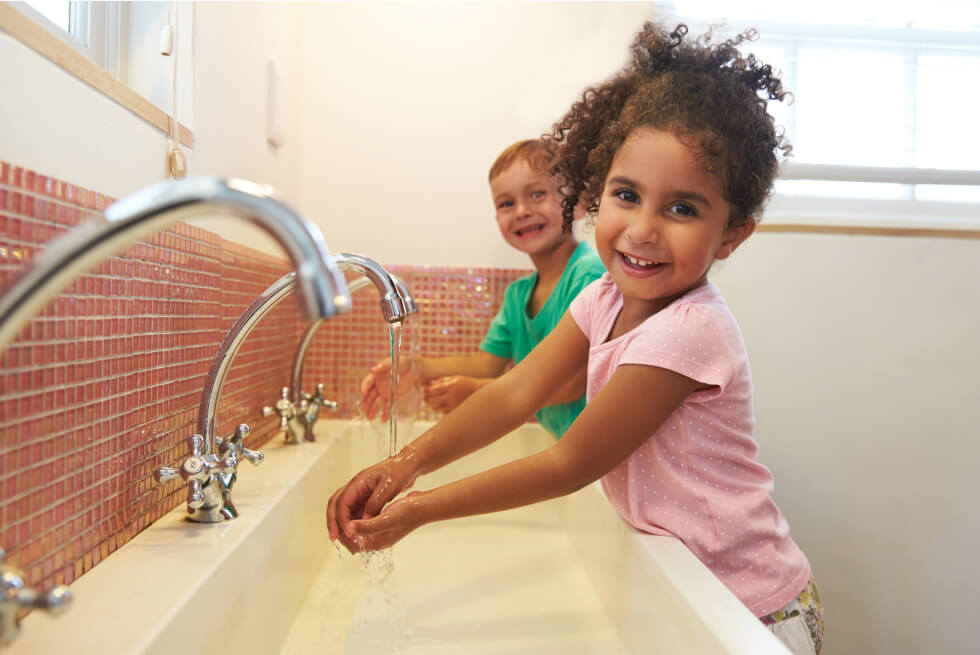 Children standing at a sink and washing their hands.