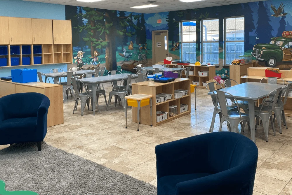 Classroom with tables and chairs, cubbies, and a campsite mural on the wall.