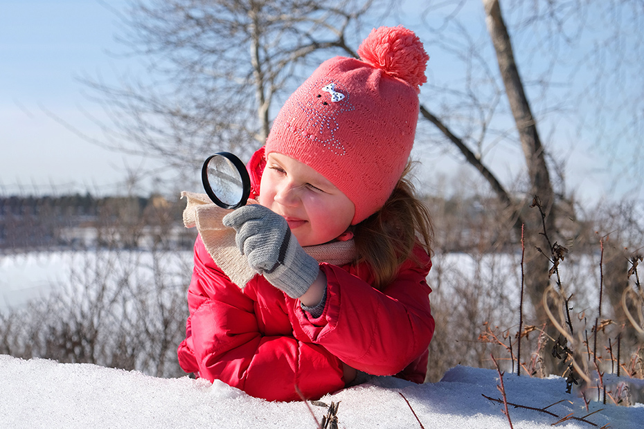 Girl with magnifying glass exploring winter.